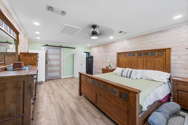 bedroom with light wood-type flooring, a barn door, and wooden walls