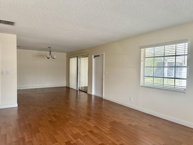 unfurnished room with a chandelier, a textured ceiling, and dark hardwood / wood-style flooring