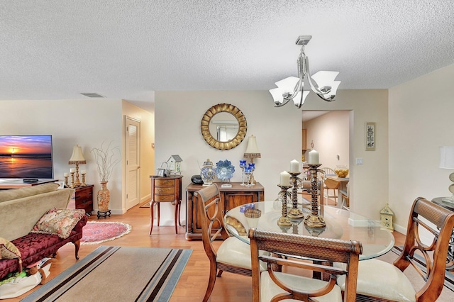 dining area with a textured ceiling, a notable chandelier, and light hardwood / wood-style floors