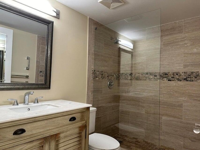 bathroom featuring a tile shower, vanity, and toilet