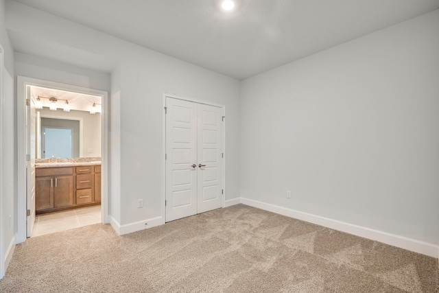 unfurnished bedroom with light colored carpet, sink, connected bathroom, and a closet