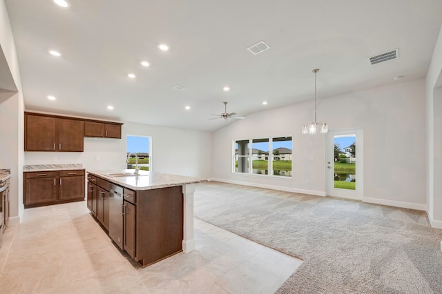 kitchen featuring light stone counters, ceiling fan with notable chandelier, light colored carpet, sink, and pendant lighting