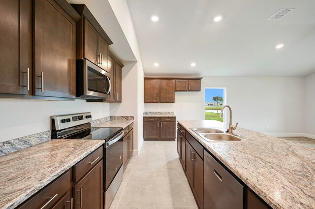 kitchen with light stone countertops, appliances with stainless steel finishes, dark brown cabinetry, sink, and light tile patterned floors