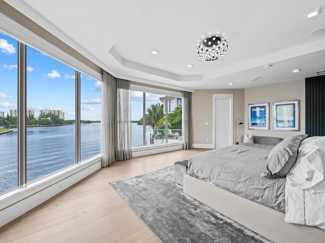 bedroom featuring visible vents, a baseboard radiator, a water view, a tray ceiling, and light wood-type flooring