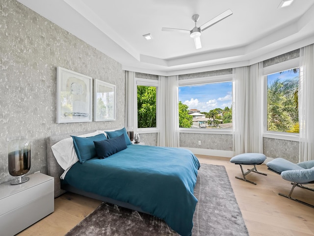 bedroom with a ceiling fan, a tray ceiling, wallpapered walls, and wood finished floors