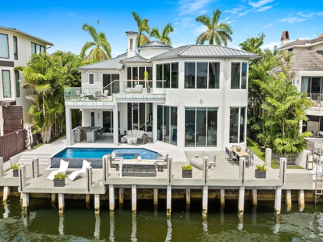 rear view of property with outdoor lounge area, a standing seam roof, a deck with water view, metal roof, and a balcony