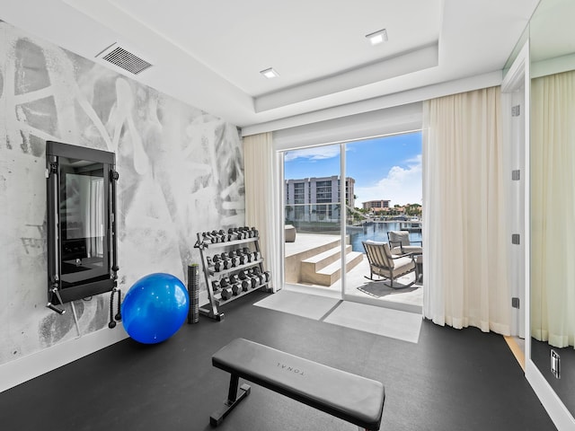 workout area featuring a tray ceiling, visible vents, and a water view