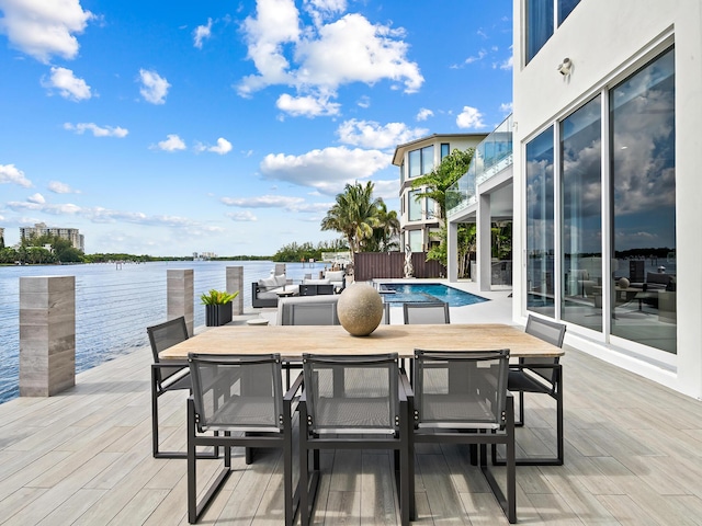 wooden terrace with outdoor dining space, a water view, and an outdoor pool