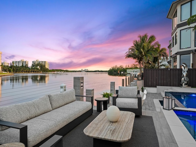 patio terrace at dusk featuring a fenced in pool, a water view, and an outdoor hangout area