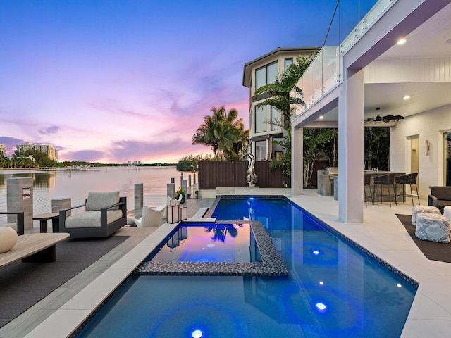 view of swimming pool featuring ceiling fan, a water view, fence, a pool with connected hot tub, and outdoor dry bar