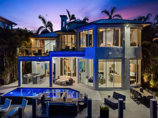 back of house at dusk with a balcony, metal roof, outdoor dry bar, a standing seam roof, and an outdoor living space