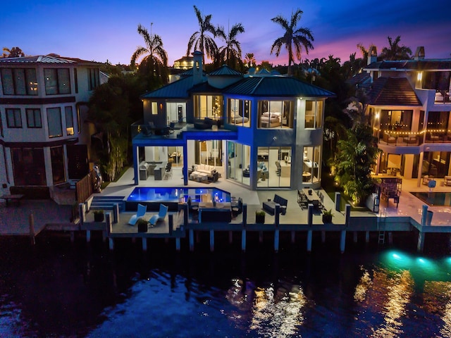 back of house at dusk featuring a patio, metal roof, an outdoor hangout area, a water view, and an outdoor pool