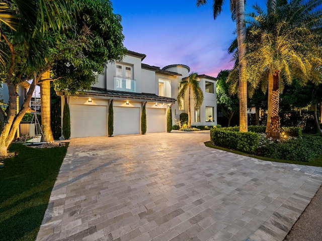 mediterranean / spanish house featuring metal roof, an attached garage, a standing seam roof, decorative driveway, and stucco siding