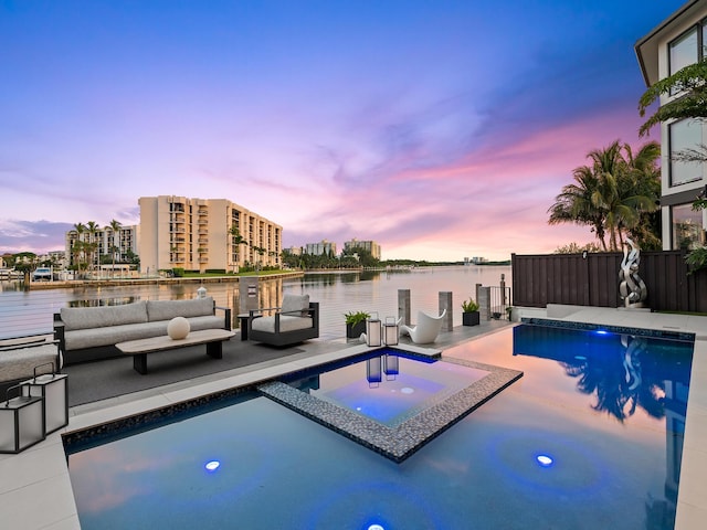 pool at dusk with an outdoor hangout area, a patio, a water view, and a pool with connected hot tub