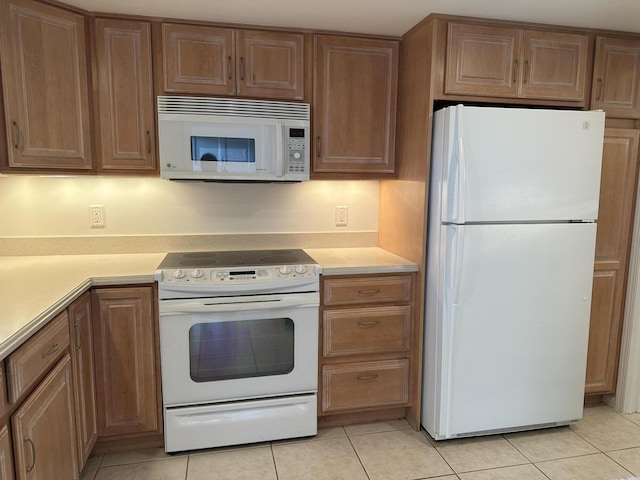 kitchen with light tile patterned floors, light countertops, white appliances, and brown cabinetry