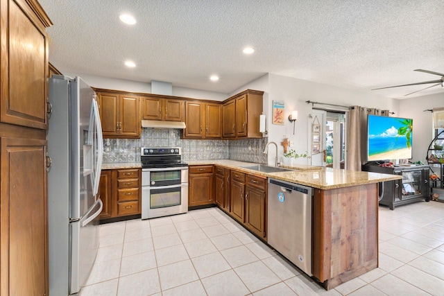 kitchen featuring appliances with stainless steel finishes, sink, kitchen peninsula, light stone countertops, and a textured ceiling