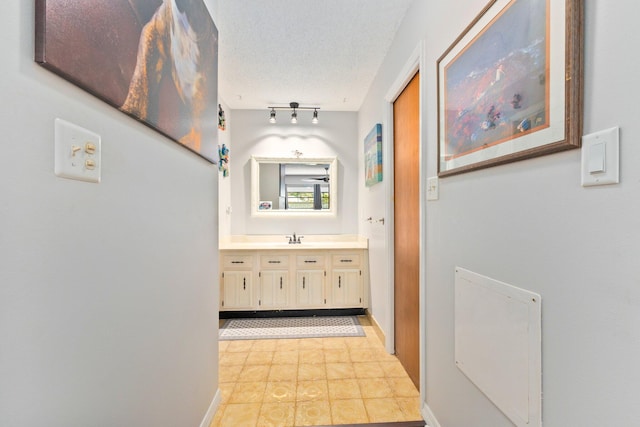 corridor with rail lighting, sink, and a textured ceiling