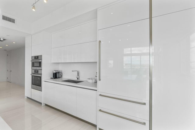 kitchen with sink, white cabinetry, double oven, and light tile patterned floors