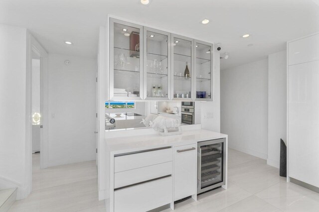 bar featuring white cabinetry, beverage cooler, light tile patterned floors, and oven