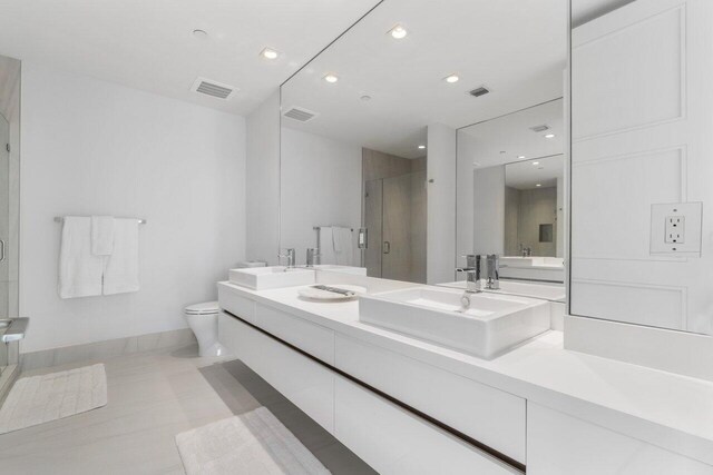 bathroom with tile patterned flooring, a shower with door, vanity, and toilet