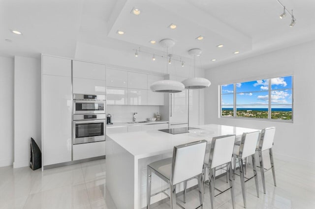 kitchen featuring double oven, a breakfast bar, a sink, white cabinets, and a center island