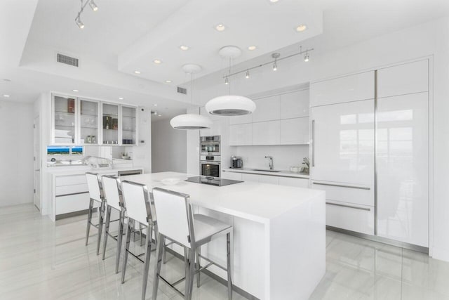 kitchen with hanging light fixtures, white cabinets, sink, a center island, and double oven