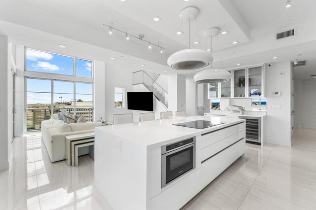 kitchen with white cabinets, hanging light fixtures, track lighting, and an island with sink