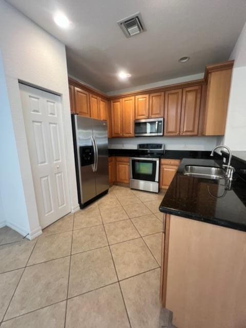 kitchen with sink, light tile patterned floors, appliances with stainless steel finishes, and dark stone counters