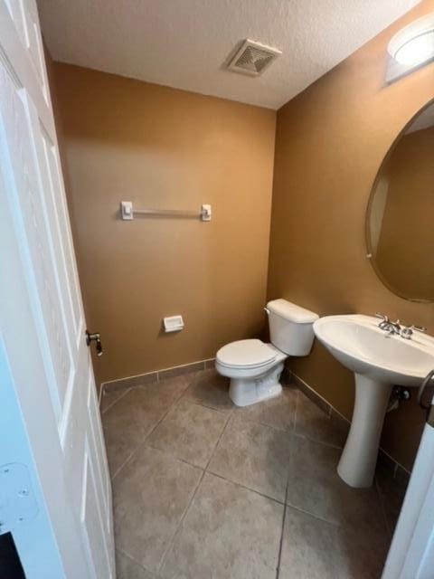 bathroom featuring a textured ceiling, toilet, sink, and tile patterned flooring