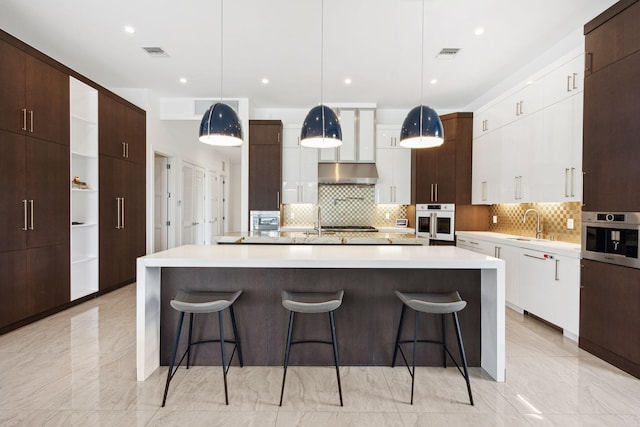 kitchen featuring a large island with sink, oven, exhaust hood, and decorative light fixtures