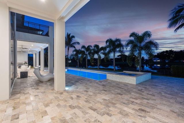 pool at dusk with a patio and a hot tub