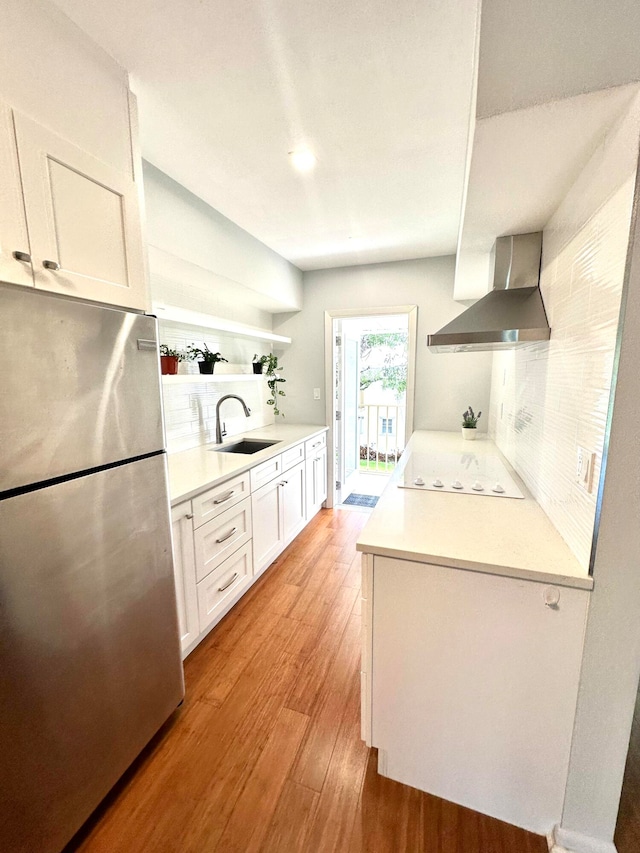 kitchen with white electric cooktop, stainless steel fridge, wall chimney exhaust hood, sink, and light wood-type flooring