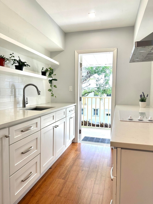 bar with white electric cooktop, sink, light wood-type flooring, and white cabinetry