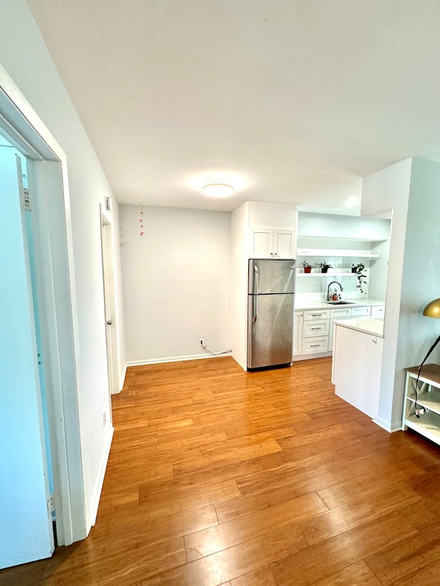 kitchen featuring stainless steel refrigerator, sink, light wood-type flooring, and white cabinetry