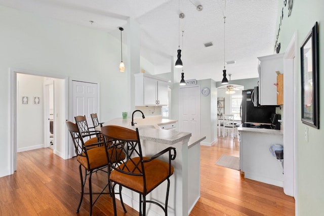 kitchen with kitchen peninsula, ceiling fan, decorative light fixtures, light hardwood / wood-style flooring, and white cabinets