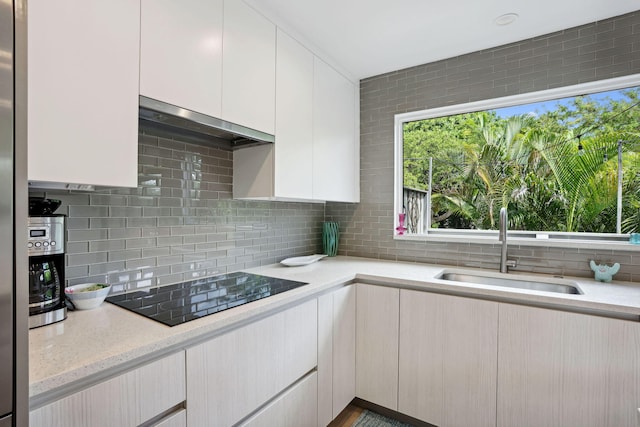 kitchen with light stone countertops, tasteful backsplash, sink, white cabinetry, and black electric stovetop