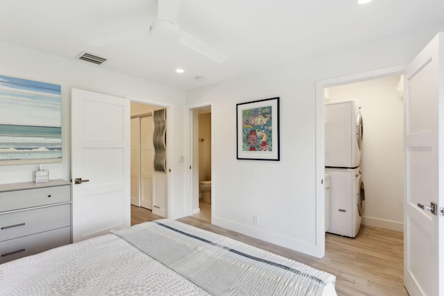 bedroom with ceiling fan, stacked washing maching and dryer, ensuite bathroom, and light hardwood / wood-style flooring