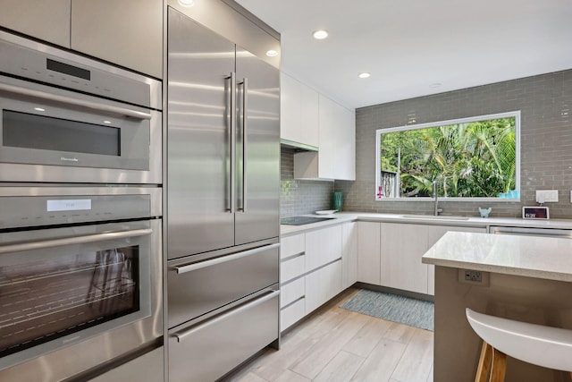 kitchen featuring stainless steel appliances, sink, decorative backsplash, and light hardwood / wood-style floors