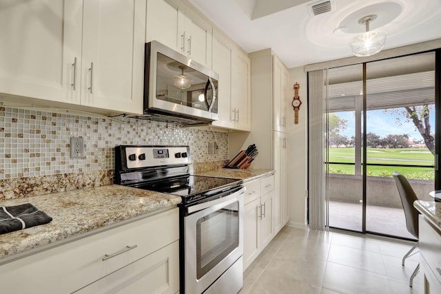 kitchen featuring tasteful backsplash, white cabinets, appliances with stainless steel finishes, light stone counters, and light tile patterned flooring