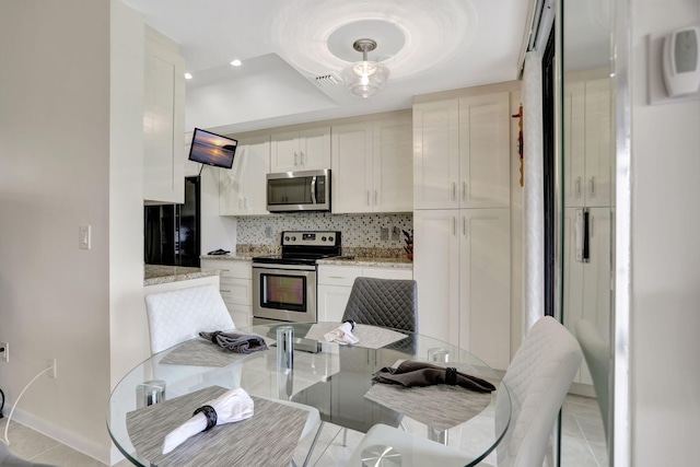 kitchen with appliances with stainless steel finishes, backsplash, white cabinetry, light stone counters, and light tile patterned flooring