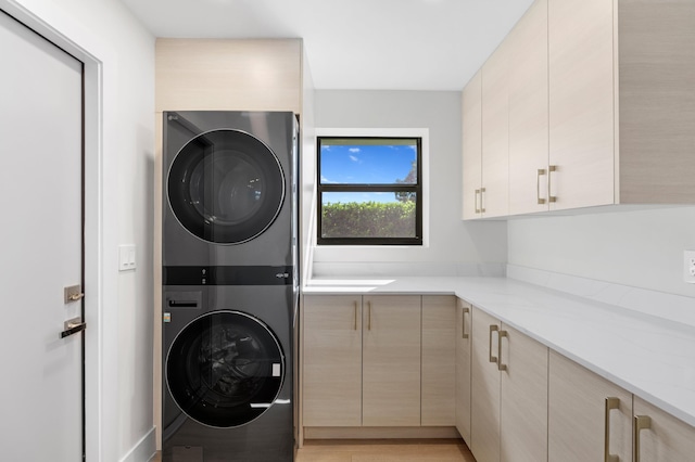 washroom featuring cabinets, light hardwood / wood-style flooring, and stacked washer / dryer