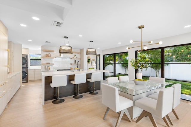 dining space featuring an inviting chandelier, light hardwood / wood-style floors, stacked washer / drying machine, and sink