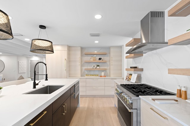 kitchen featuring light hardwood / wood-style floors, pendant lighting, stainless steel stove, sink, and wall chimney range hood