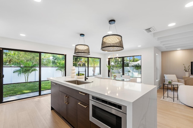 kitchen with hanging light fixtures, a center island with sink, sink, and plenty of natural light