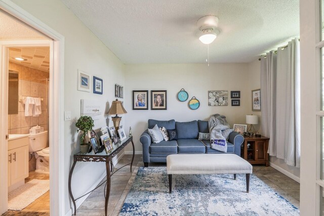 living room featuring a textured ceiling, ceiling fan, and light tile patterned floors