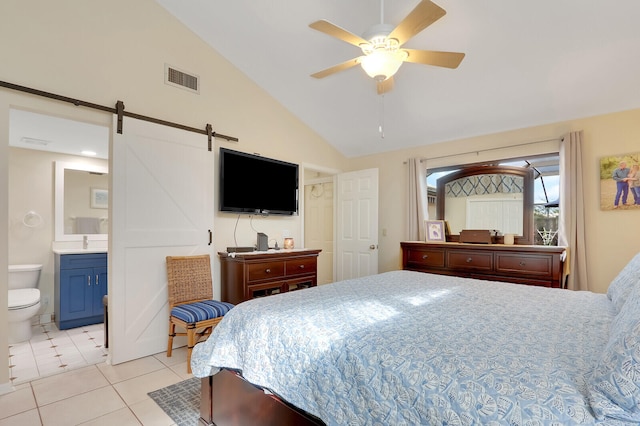 bedroom with ceiling fan, light tile patterned flooring, connected bathroom, a barn door, and vaulted ceiling