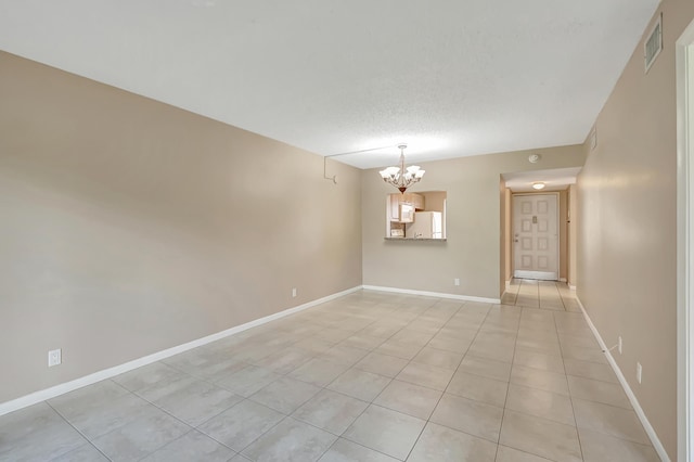 unfurnished room featuring a chandelier, a textured ceiling, light tile patterned flooring, visible vents, and baseboards