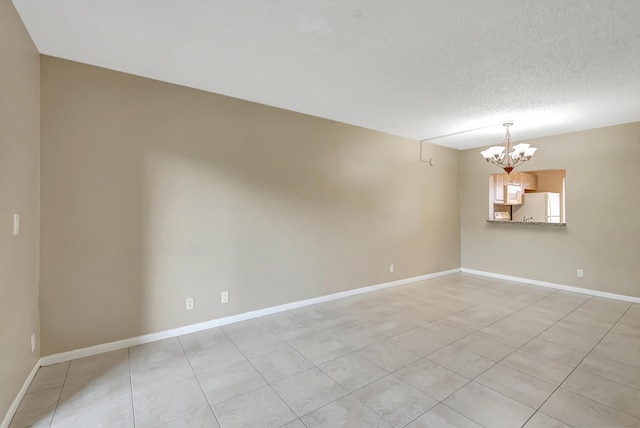 empty room featuring an inviting chandelier, baseboards, and a textured ceiling