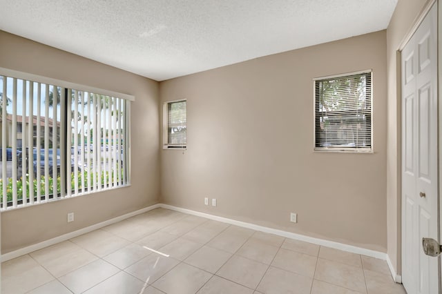 spare room with light tile patterned flooring, a textured ceiling, and baseboards