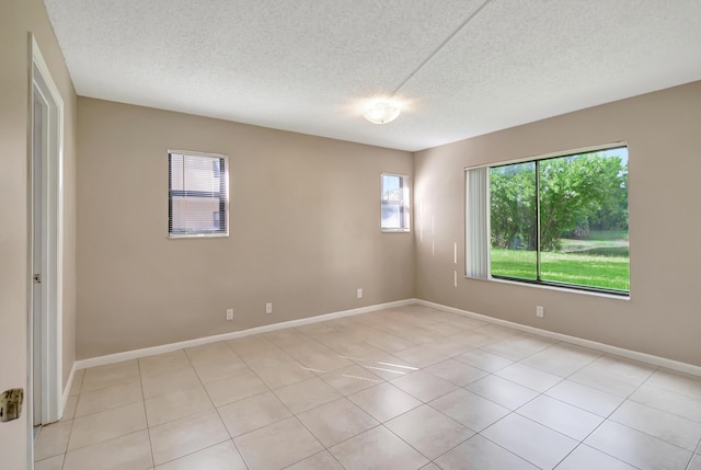 empty room featuring a textured ceiling, light tile patterned floors, and baseboards